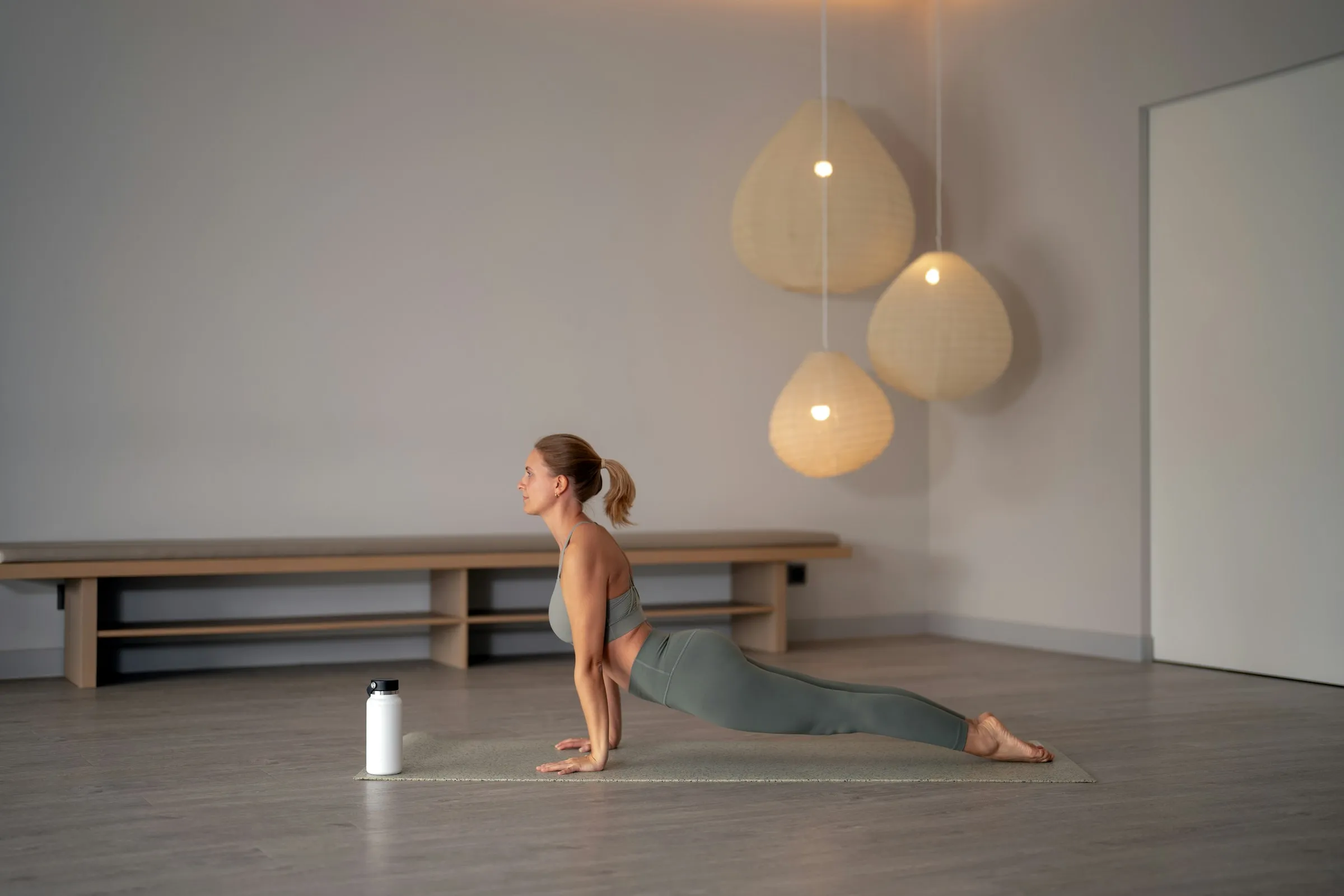 Mujer en postura de cobra sobre un mat en un estudio de yoga amplio, de tonos claros y lámparas de fibra natural.